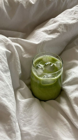 A glass of iced matcha resting on white linen bedding